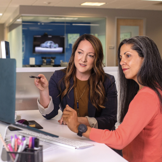 Two women are sitting, looking at a monitor and discussing something